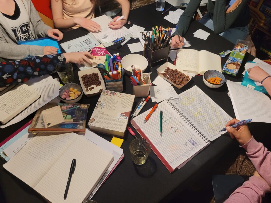Der chaotische Tisch einer Schreibgruppe. Mehrere Notizbücher, Stifte und Zettel sind zu sehen.